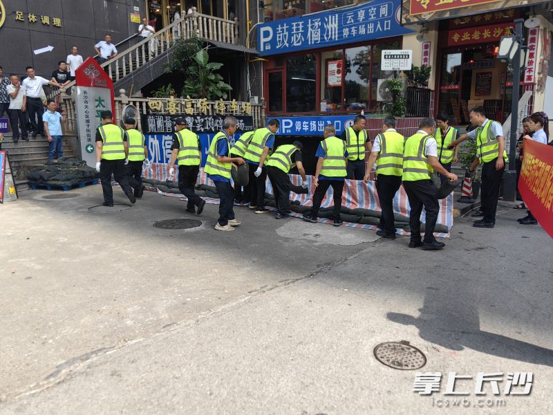 物业小区应急抢险小组成员迅速行动，用沙袋、挡水板等防汛物资在地下车库出入口筑起防水墙。