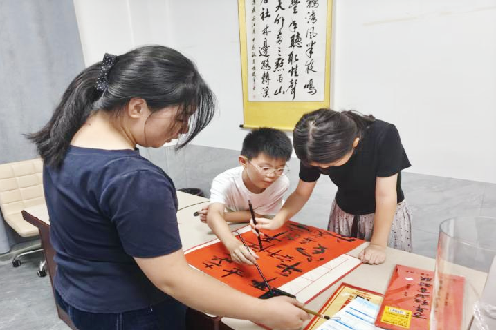 笔墨飘香的活动室里,志愿者俯身握笔指点,少年认真学习书法。 笔墨飘香的活动室里,志愿者俯身握笔指点,少年认真学习书法。